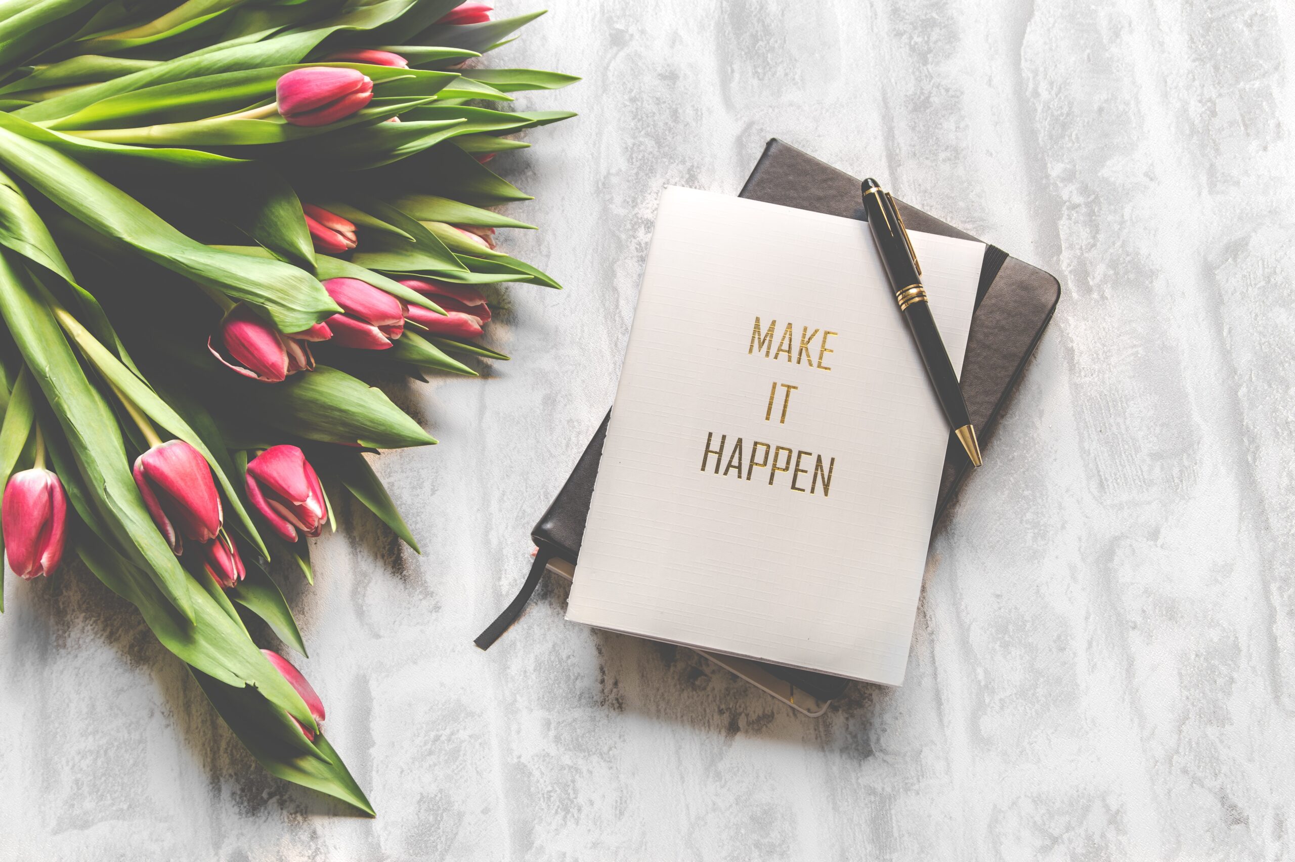 photo of notebook that says make it happen on it next to a bouquet of tulips